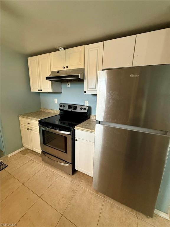 Kitchen with appliances with stainless steel finishes, white cabinetry, under cabinet range hood, and light tile patterned flooring