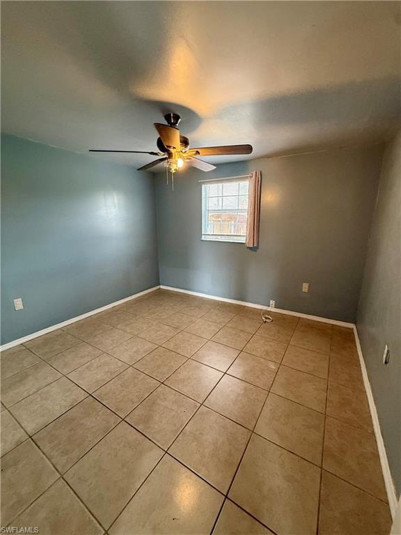 Tiled empty room featuring baseboards and a ceiling fan