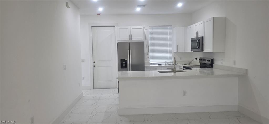 Kitchen featuring light stone counters, stainless steel appliances, white cabinets, light marble finish flooring, and a peninsula
