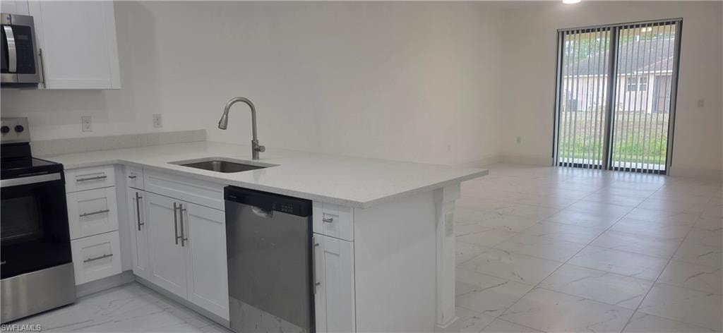 Kitchen with light marble finish flooring, appliances with stainless steel finishes, white cabinets, light stone counters, and a peninsula