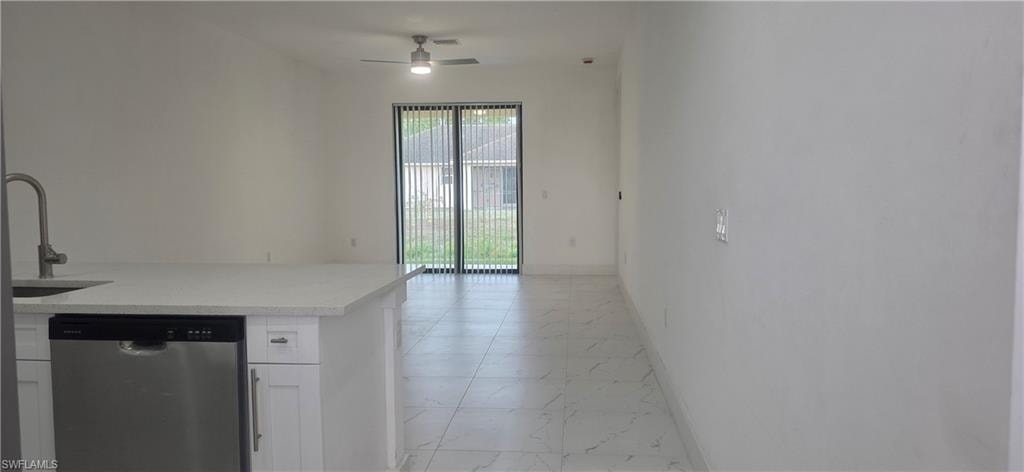 Kitchen featuring stainless steel dishwasher, white cabinets, light stone countertops, a ceiling fan, and light marble finish floors