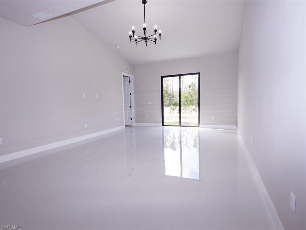 Empty room with tile patterned flooring, a chandelier, and vaulted ceiling