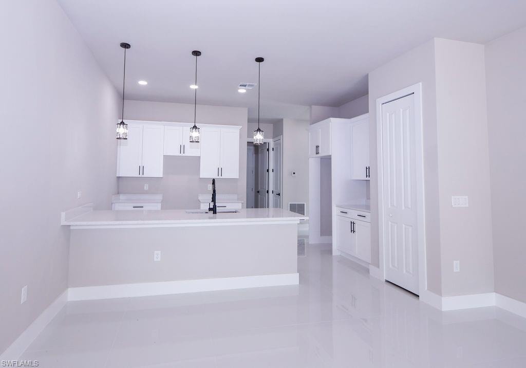 Kitchen featuring white cabinetry, a peninsula, pendant lighting, light stone counters, and a kitchen bar