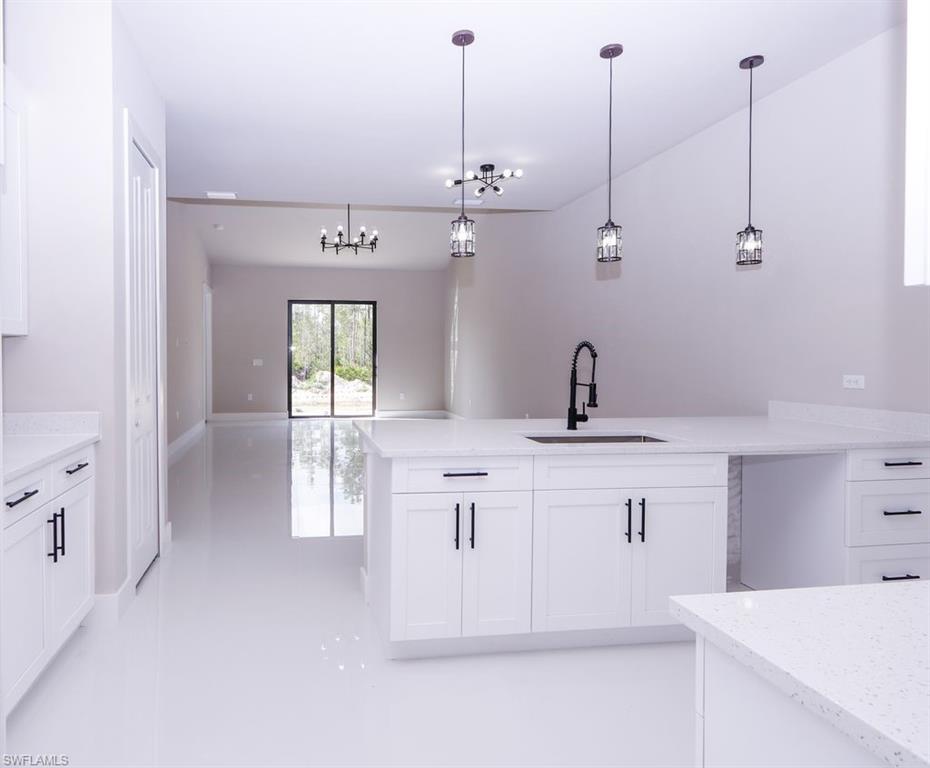 Kitchen featuring a peninsula, white cabinets, hanging light fixtures, and light stone countertops