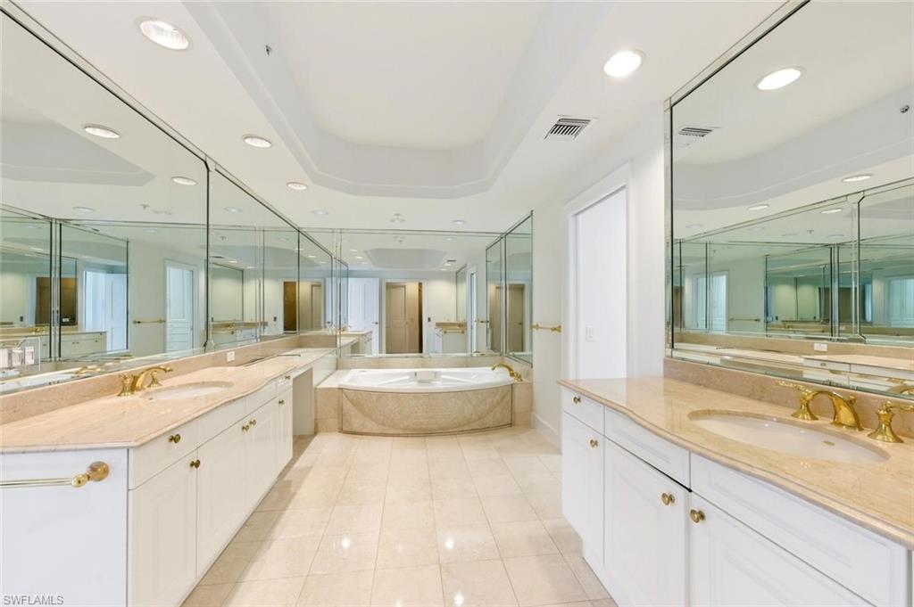 Spacious bathroom featuring a built-in corner soaking tub, dual vanities with integrated sinks, and extensive mirror coverage