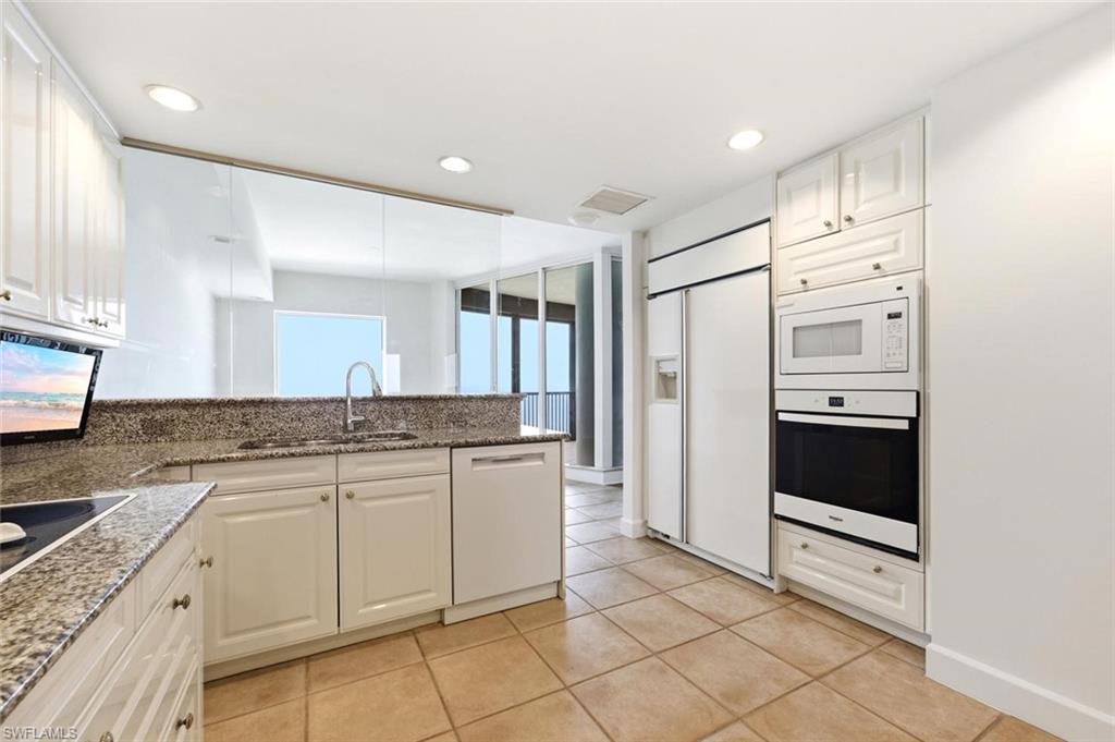 Modern kitchen featuring white cabinetry, granite countertops, tile flooring, and integrated white appliances including a refrigerator, oven, microwave, and dishwasher