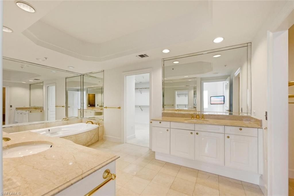 Bathroom featuring a large corner soaking tub, dual vanity sinks with light-toned countertops, extensive wall-mounted mirrors, and recessed ceiling lighting