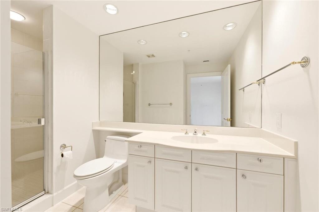 Bathroom featuring a large vanity mirror, recessed lighting, white cabinetry, a single basin sink, and a glass-enclosed shower