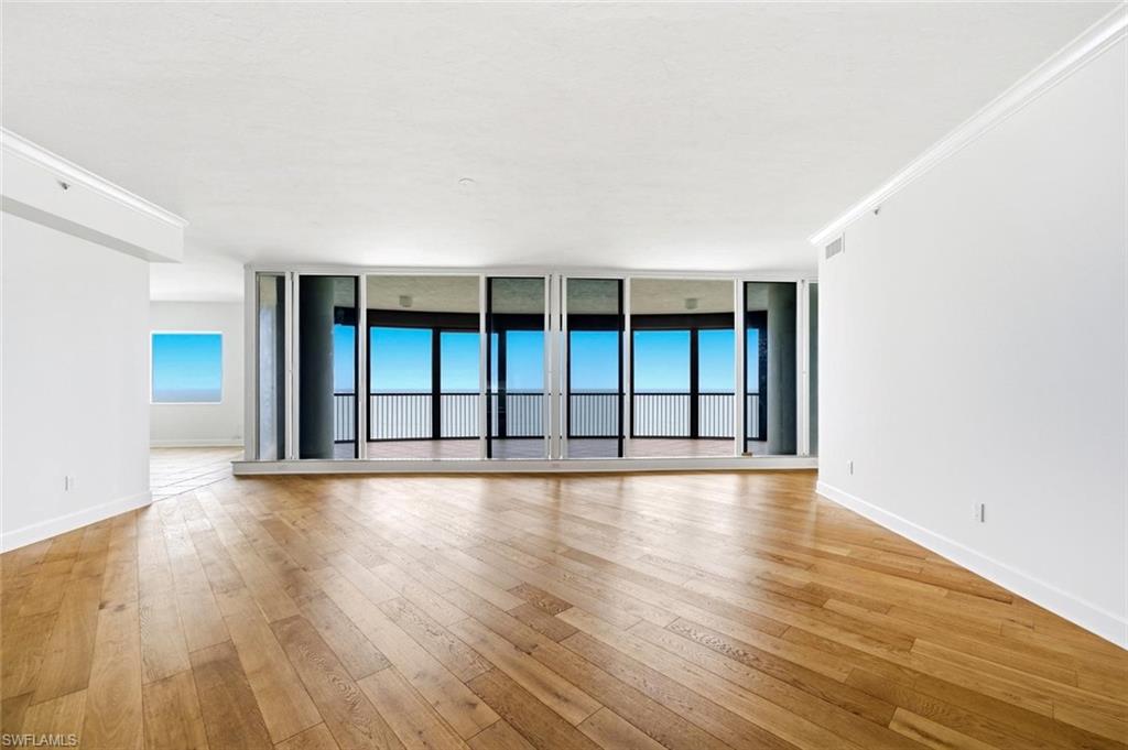 Expansive living area featuring wood-finish flooring, a full wall of floor-to-ceiling windows, and a private balcony with metal railings