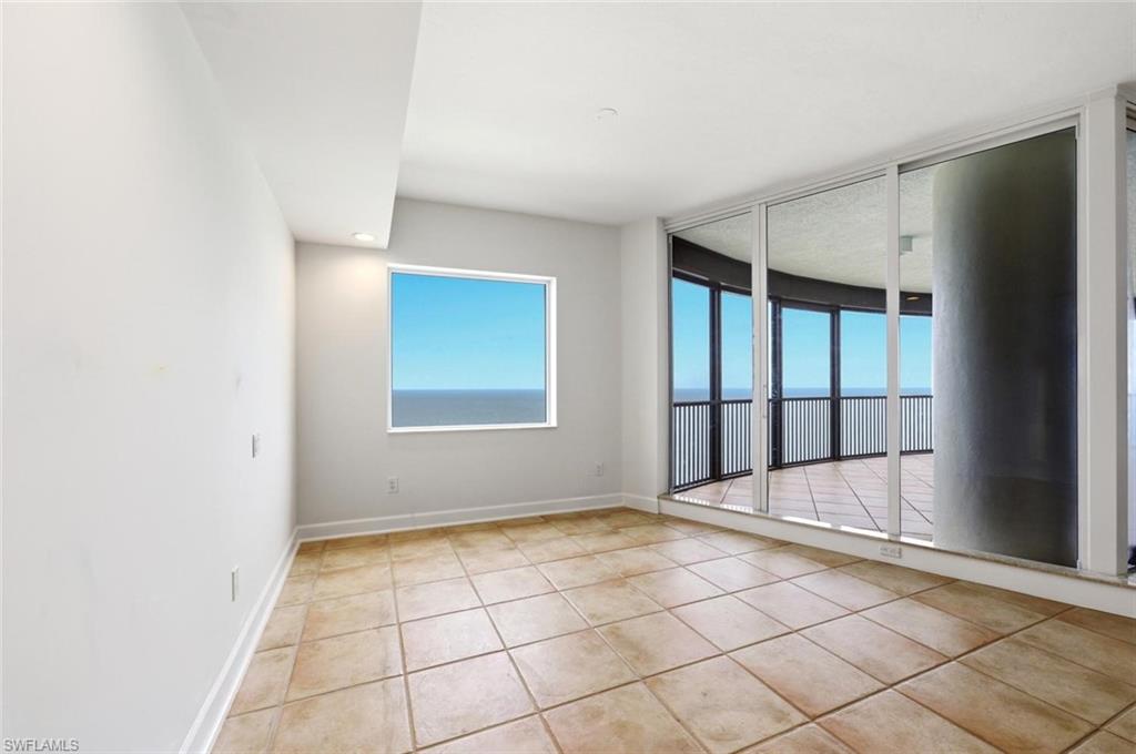 Spacious room featuring floor-to-ceiling sliding glass doors, a large picture window, and direct access to an expansive outdoor balcony with metal railings and water views