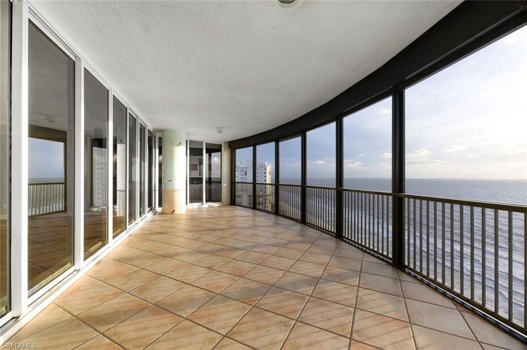 Curved balcony featuring an expansive ocean backdrop, tiled flooring, full-height sliding glass panels, and a dark metal railing