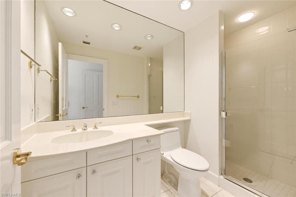 Bathroom featuring a vanity with an integrated sink, a large wall-mounted mirror, a commode, a glass-enclosed shower, and recessed lighting