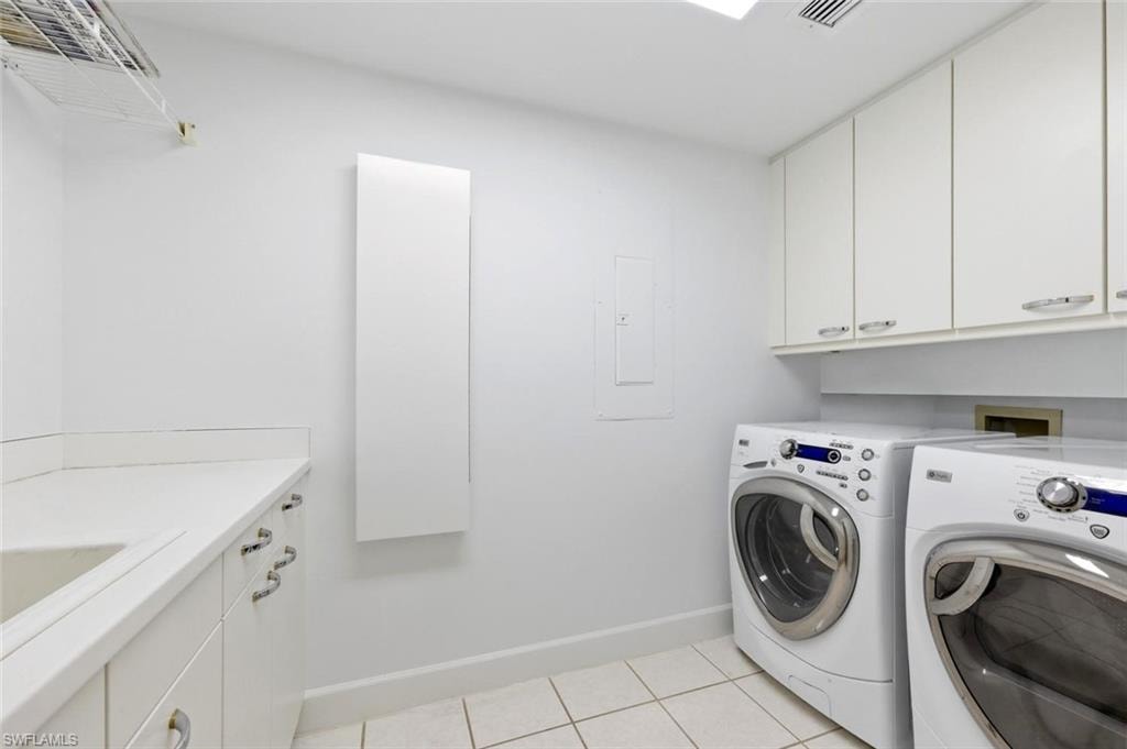 Dedicated laundry room featuring tile flooring, white cabinetry with silver hardware, a built-in sink with a white countertop, and upper storage cabinets