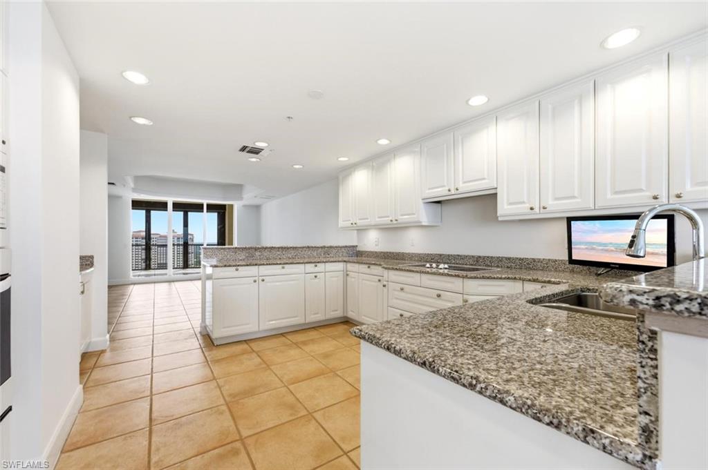 Spacious kitchen featuring white cabinetry, granite countertops, stainless steel sink, recessed lighting, and tile flooring