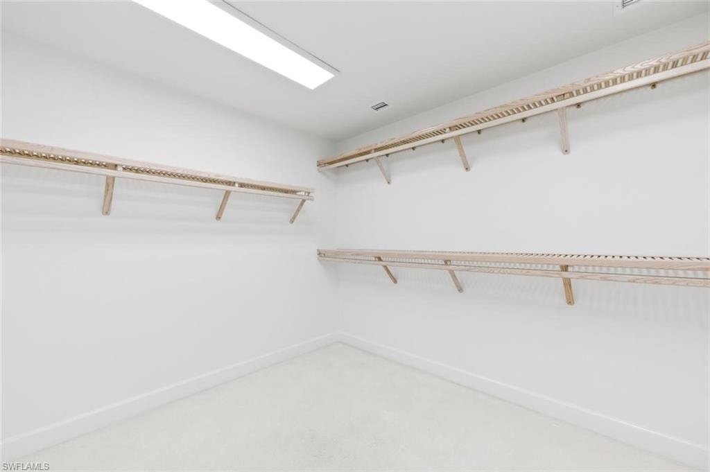 Spacious closet featuring light-toned wood shelving, white walls, and light-colored carpeting