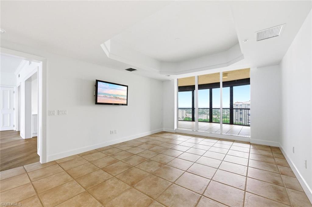 Spacious room featuring large format square tile flooring, a tray ceiling with recessed lighting, and a full-wall glass sliding door system opening to a balcony with a metal railing