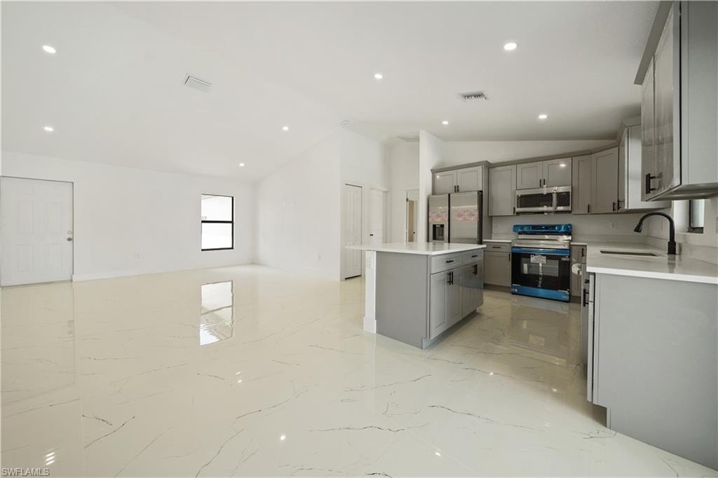 The property features an open-concept living space with polished tile flooring, recessed lighting, and a kitchen equipped with gray cabinetry, white countertops, and stainless steel appliances