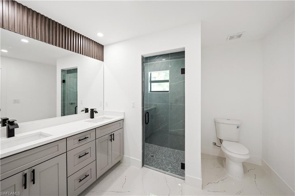 Bathroom featuring a double vanity with light gray cabinetry and black hardware, a large mirror, and a glass-enclosed shower with dark gray tile