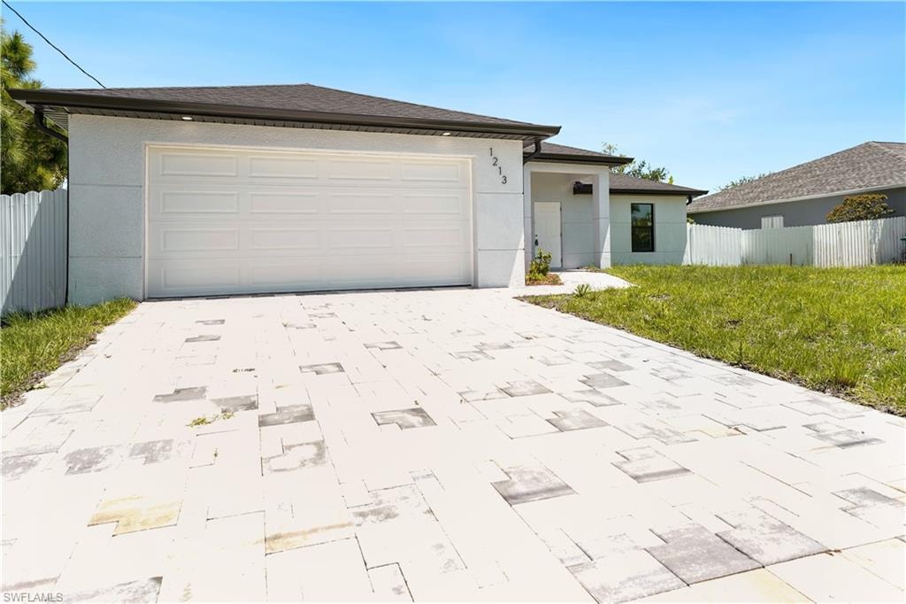 The property features a paved driveway, an attached garage, and a light-colored exterior with a dark roof