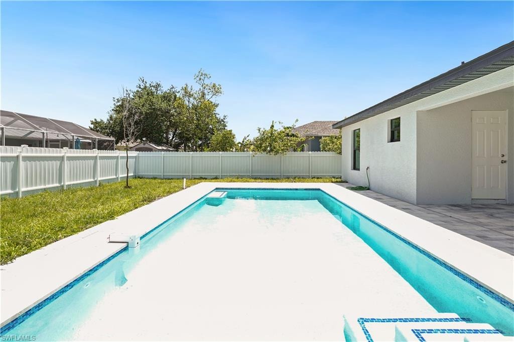 The property includes a rectangular swimming pool with a white coping and blue tile accents, a paved patio area, and a white privacy fence bordering the yard