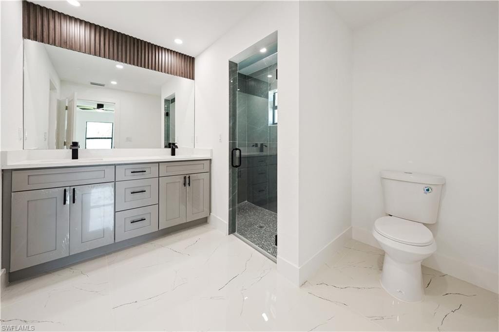 The bathroom features a double vanity with grey cabinetry, a large mirror, a glass-enclosed shower, and a toilet