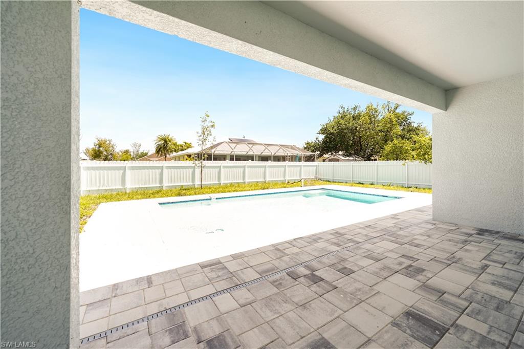 The property features a swimming pool with a surrounding white concrete deck, alongside a spacious covered patio with grey paver flooring