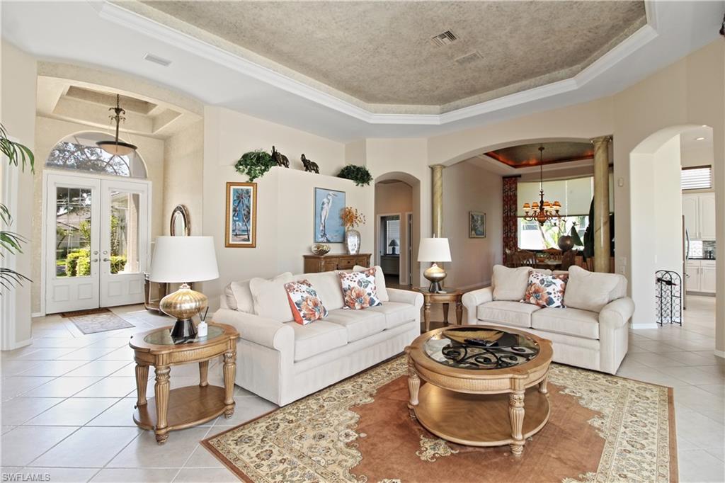 Living area with a tray ceiling, arched walkways, a chandelier, light tile patterned floors, and ornamental molding