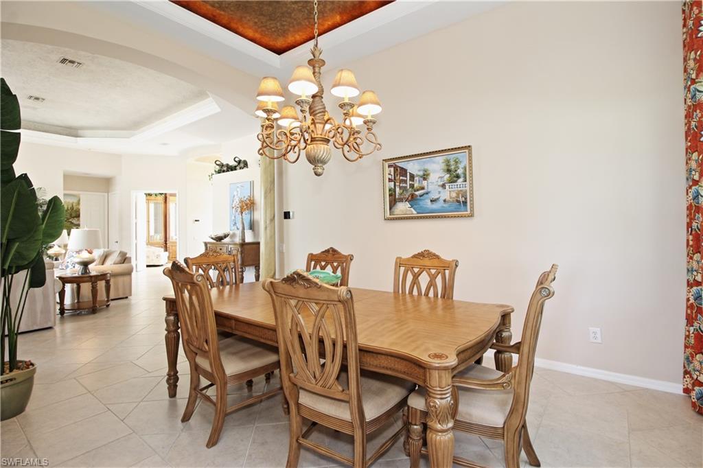 Dining area featuring arched walkways, a tray ceiling, a chandelier, crown molding, and light tile patterned flooring