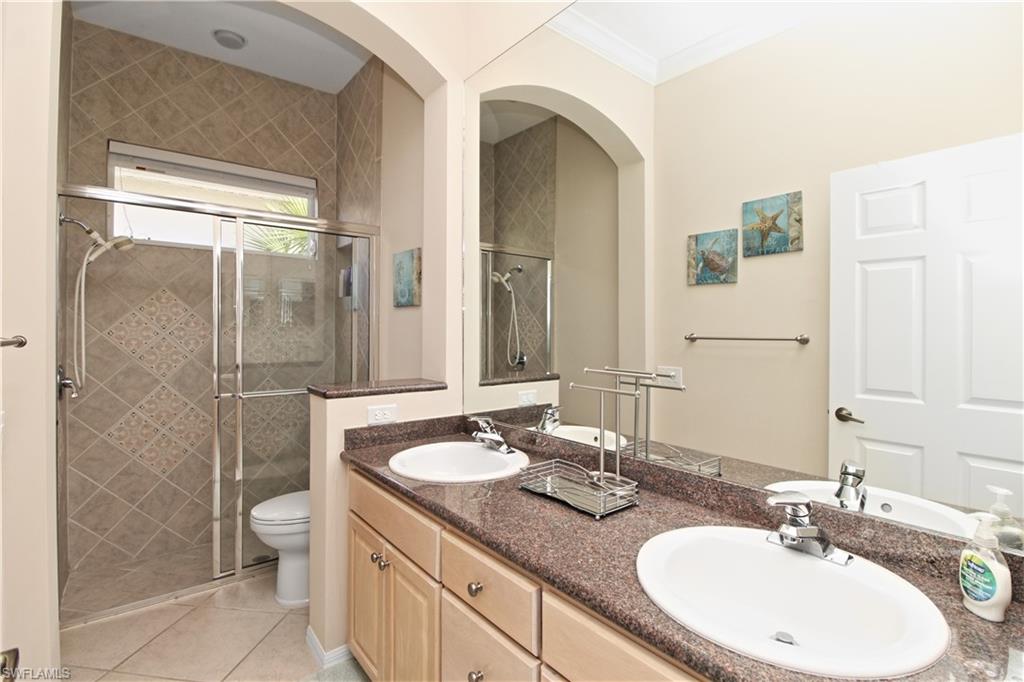 Full bathroom featuring a shower stall, double vanity, light tile patterned floors, and ornamental molding
