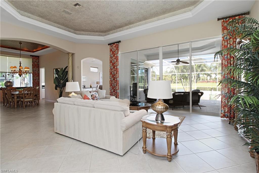 Tiled living area with a tray ceiling, arched walkways, plenty of natural light, a chandelier, and a textured ceiling