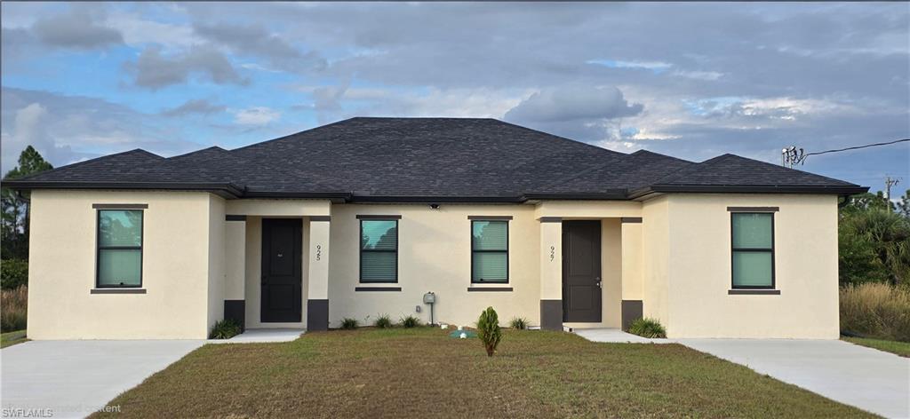 View of front of property with stucco siding, a front lawn, and roof with shingles