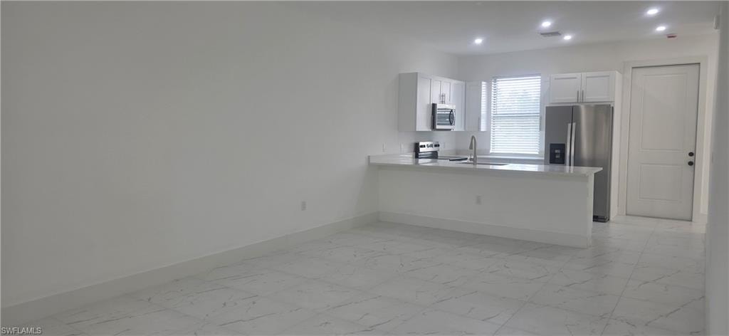 Kitchen with light marble finish floors, appliances with stainless steel finishes, a peninsula, white cabinetry, and recessed lighting