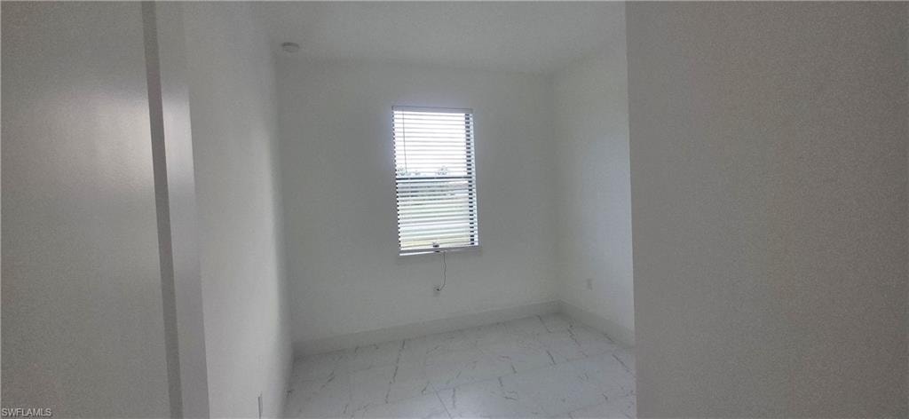 Spare room featuring light marble finish floors and baseboards