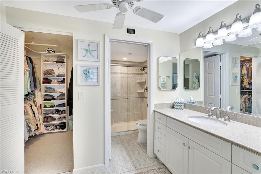 Bathroom featuring a spacious closet, vanity, a stall shower, light tile patterned flooring, and a ceiling fan