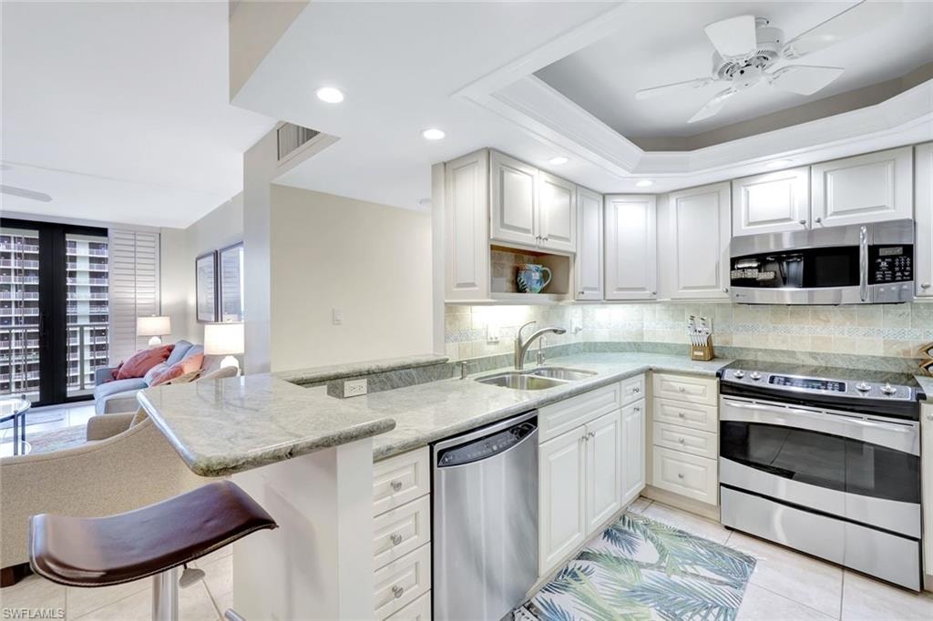 Kitchen with stainless steel appliances, light tile patterned floors, light stone countertops, ceiling fan, and recessed lighting