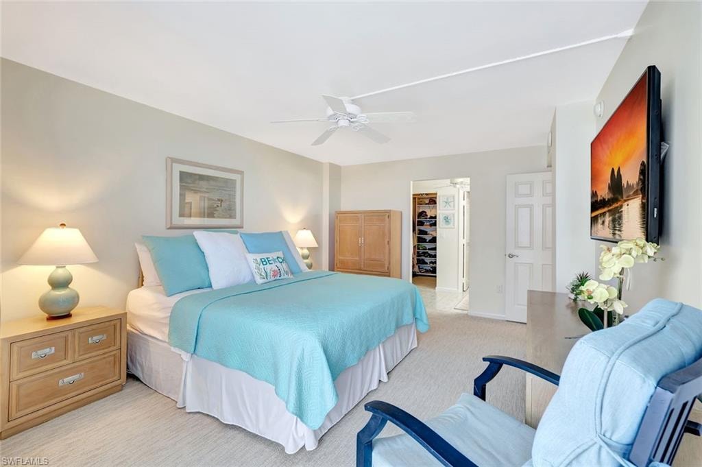 Bedroom with a spacious closet, a ceiling fan, and light carpet