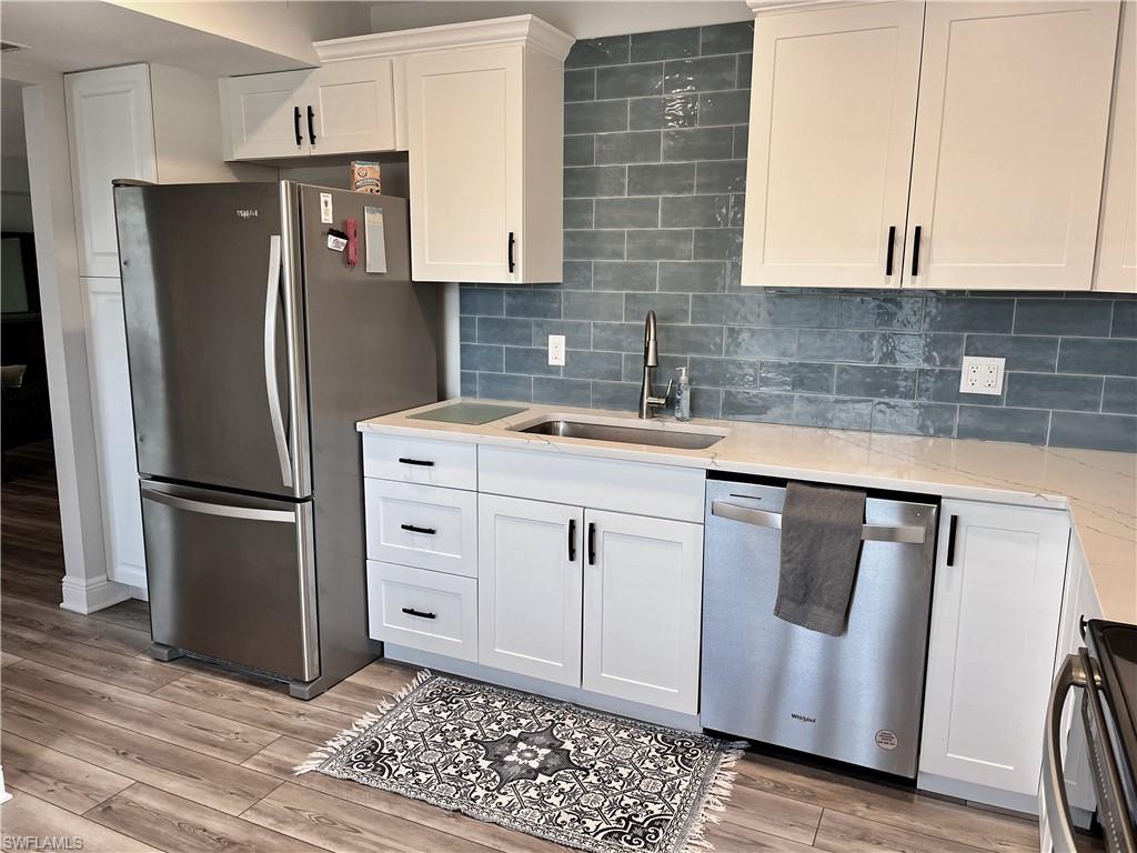Kitchen with light hardwood / wood-style flooring, stainless steel appliances, tasteful backsplash, white cabinetry, and sink