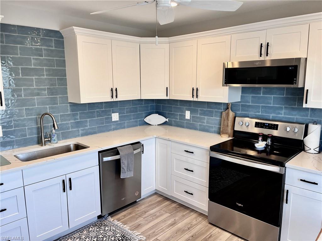 Kitchen with stainless steel appliances, backsplash, ceiling fan, light wood-type flooring, and white cabinets