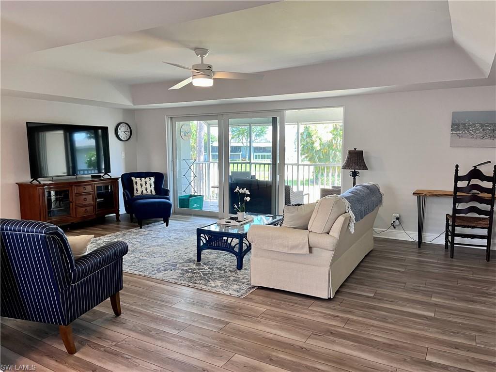 Living room with ceiling fan, a raised ceiling, and hardwood / wood-style flooring