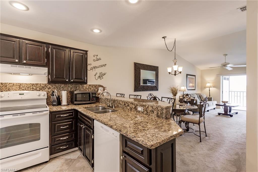 Kitchen with ceiling fan with notable chandelier, white appliances, kitchen peninsula, sink, and lofted ceiling