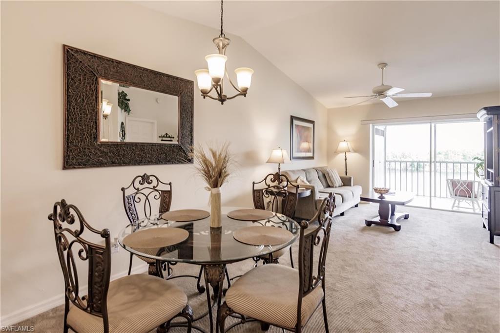 Carpeted dining room with ceiling fan with notable chandelier and lofted ceiling