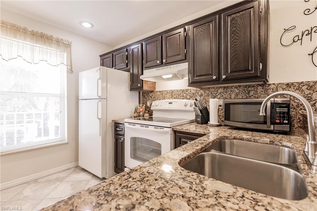Kitchen with white appliances, light stone countertops, sink, dark brown cabinets, and light tile patterned flooring