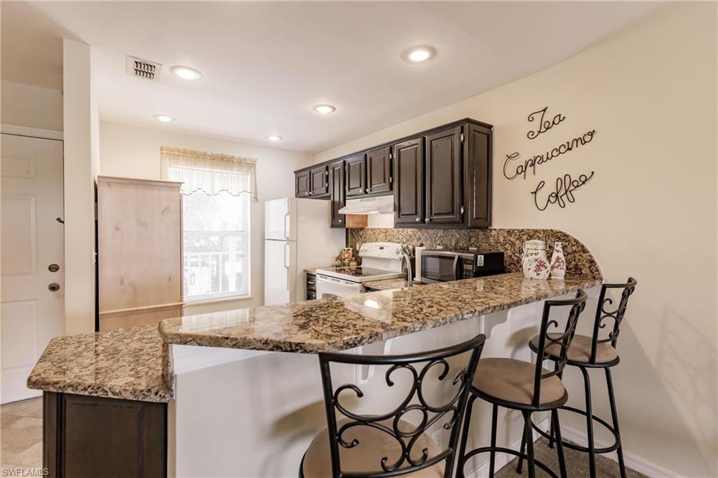 Kitchen with light stone counters, white appliances, a breakfast bar area, and kitchen peninsula
