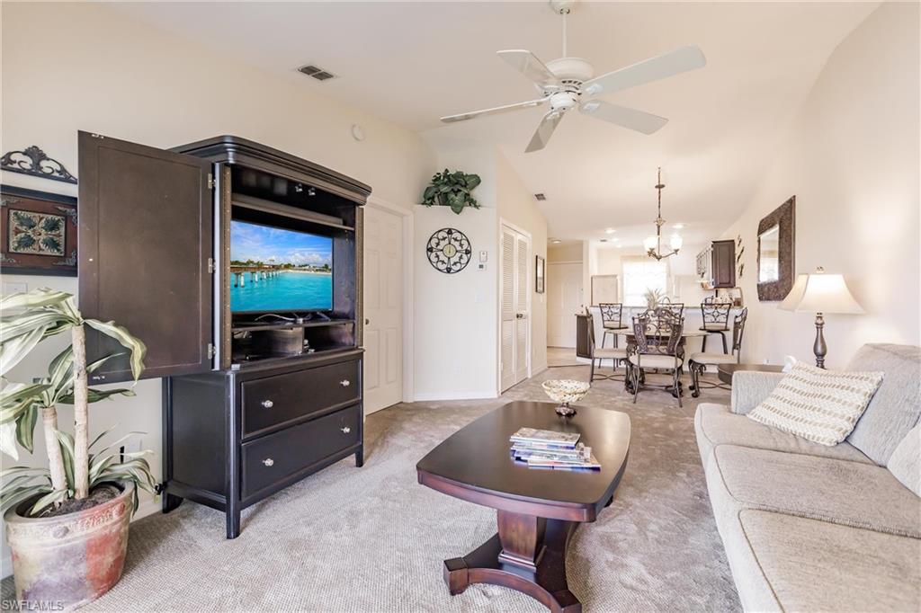 Carpeted living room featuring lofted ceiling and ceiling fan with notable chandelier