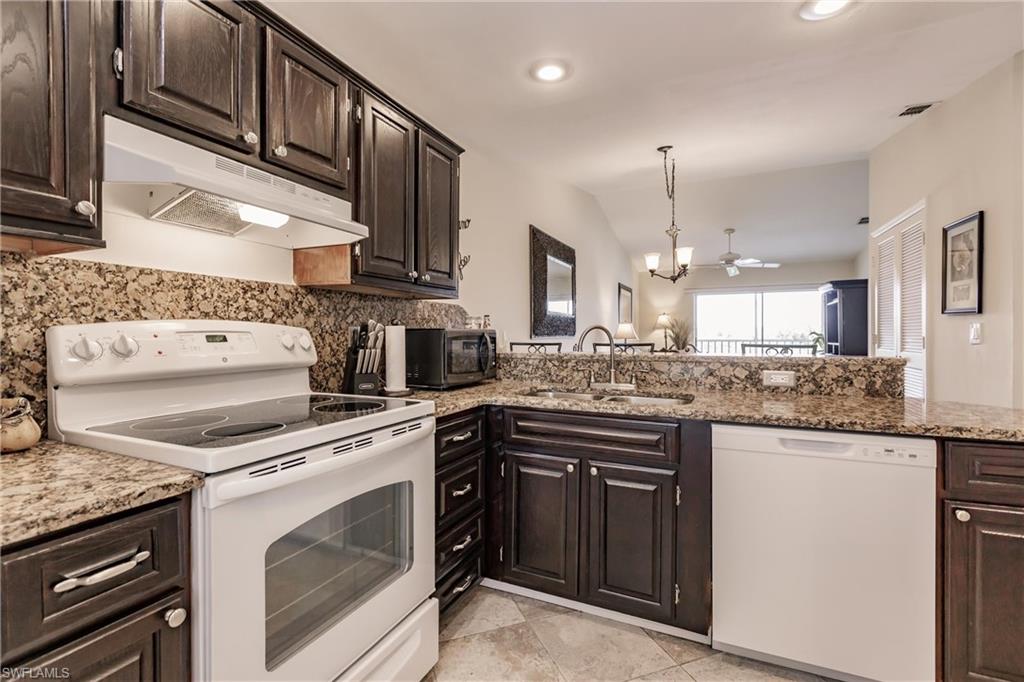 Kitchen featuring vaulted ceiling, light stone countertops, white appliances, sink, and dark brown cabinetry