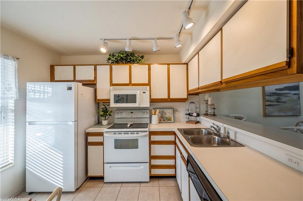 Kitchen featuring white appliances, light countertops, brown cabinetry, and white cabinets