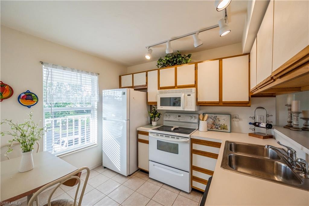 Kitchen featuring white appliances, light countertops, light tile patterned flooring, and brown cabinets