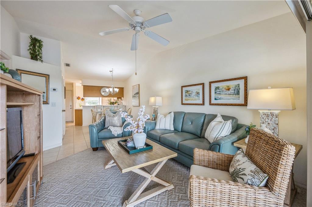 Living room featuring tile patterned flooring, ceiling fan, a chandelier, and high vaulted ceiling