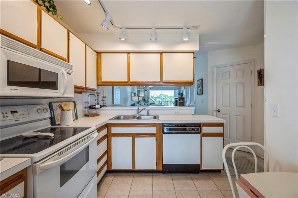 Kitchen with white appliances, white cabinets, rail lighting, light countertops, and brown cabinets