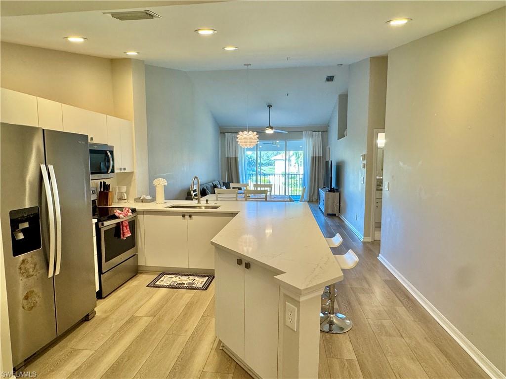 Kitchen featuring stainless steel appliances, a peninsula, a kitchen bar, white cabinets, and light wood-style floors
